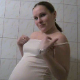 A pregnant girl rubs her big belly, takes a piss, and cleans herself off.
